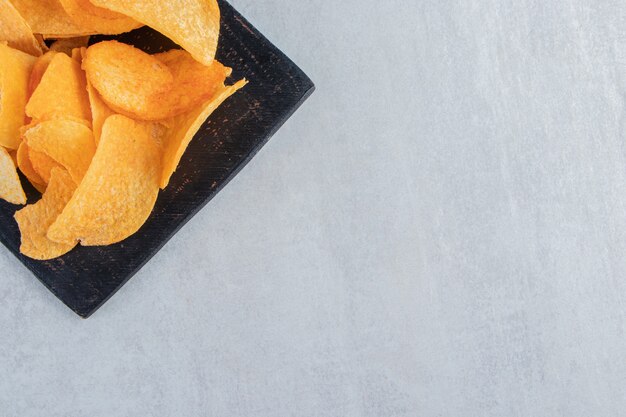 Tasty spicy potato chips on black cutting board.