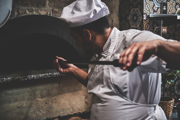 Вкусная пицца, запеченная на камне, готова, и итальянский шеф-повар вынимает ее из духовки.