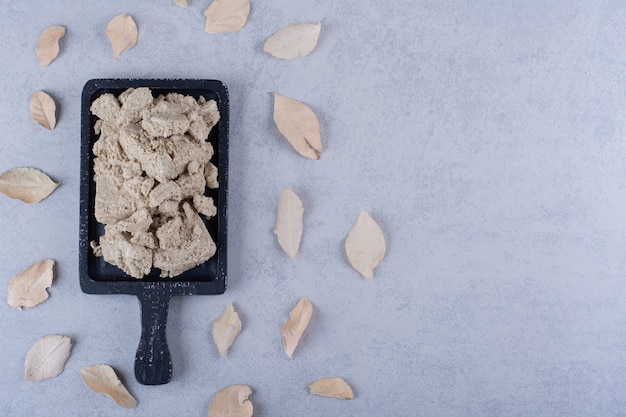 Tasty sunflower halva on black wooden board with dry leaves.