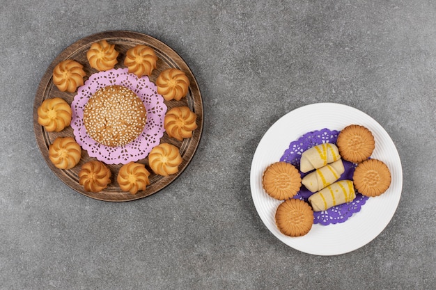 Tasty sweet biscuits and plate of cookies on marble surface.