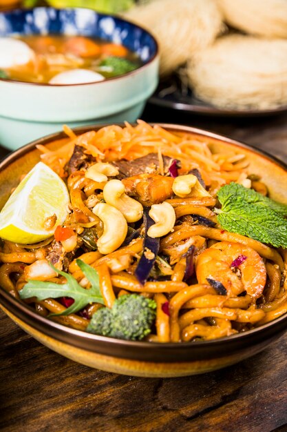 Tasty thai udon noodles with beef; broccoli; mint; nuts and lemon in bowl on wooden table