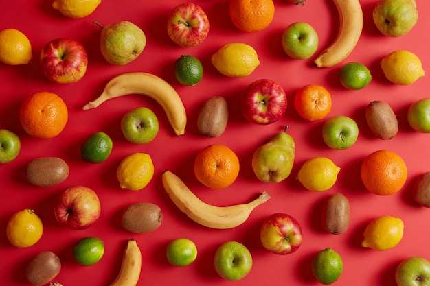 Free photo tasty tropical and domestic fruits collected from orchard. delicious appetizing banana, kiwi, apple, pear and lemon on red background. assortment of healthy beneficial natural products. flat lay