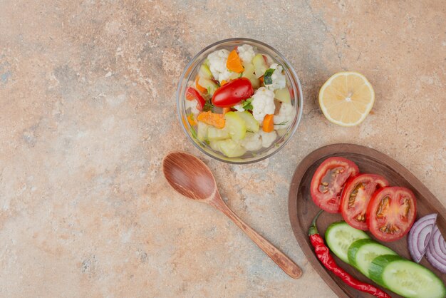 Tasty vegetables on glass plate with wooden board of tomato, cucumber and onion on marble