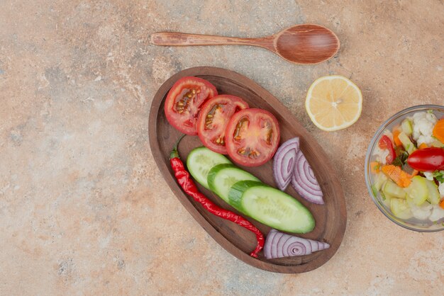 Tasty vegetables on glass plate with wooden board of tomato, cucumber and onion on marble