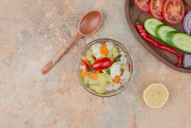 Вкусные овощи на стеклянной тарелке с деревянной доской из помидоров, огурцов и лука на мраморе