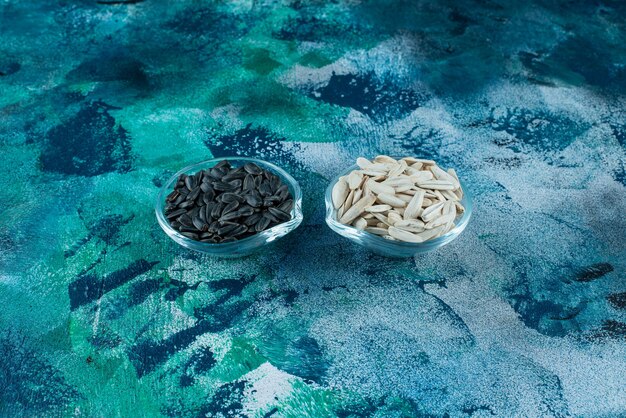 Tasty white and black sunflower seeds in a glass bowls , on the blue table.