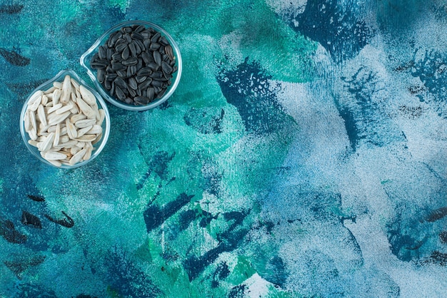 Tasty white and black sunflower seeds in a glass bowls on blue. 