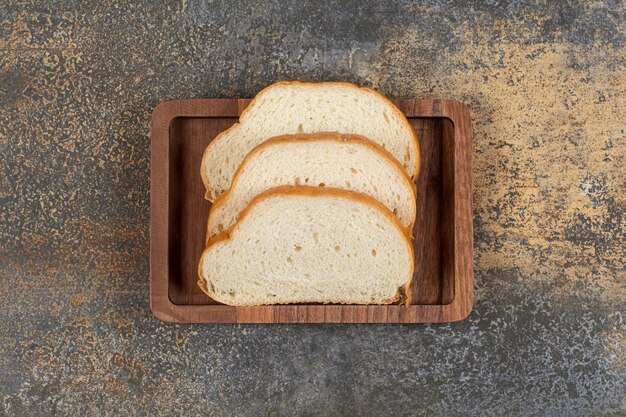 Tasty white bread slices on wooden plate.