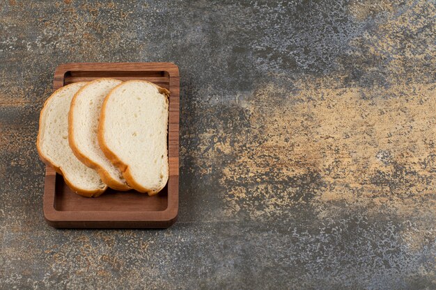 Tasty white bread slices on wooden plate.