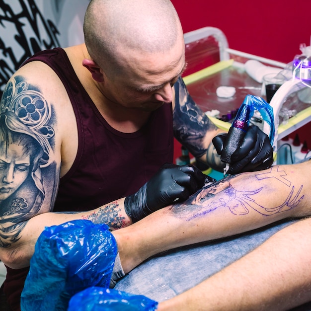 Tattoo master painting on leg with machine