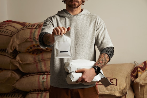 Tattooed barista holds blank package bags with freshly baked coffee beans ready for sale and deliverybrewing
