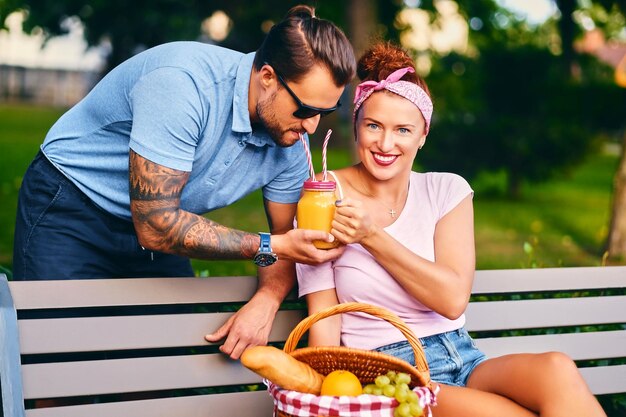 入れ墨のあるひげを生やした男性と赤毛の女性が公園のベンチでピクニックをしています。