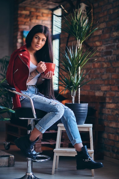 Tattooed brunette female drinks hot coffee in a room with loft interior.