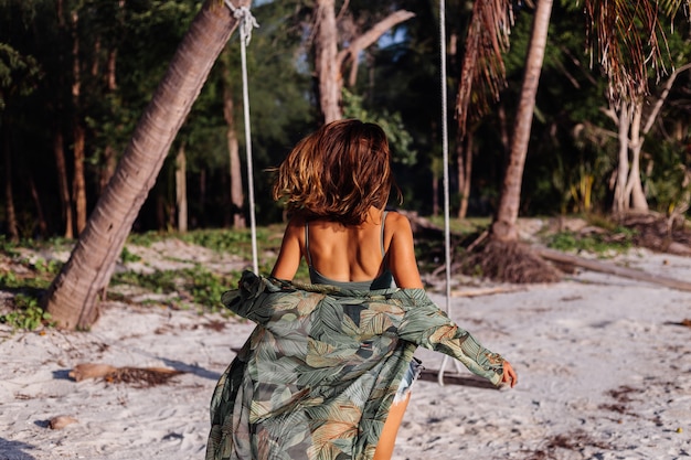 tattooed caucasian woman in denim shorts and green trendy crop top in the beach