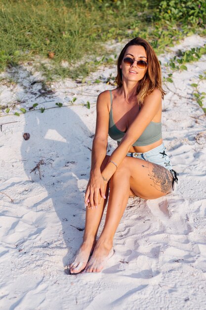 tattooed caucasian woman in denim shorts and green trendy crop top