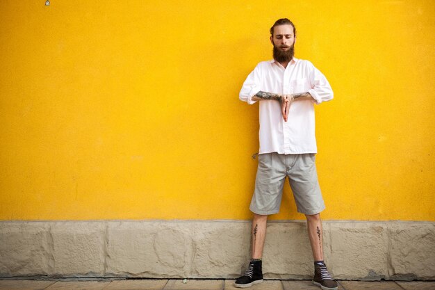 Tattooed fashion bearded hipster on yellow wall posing outdoor