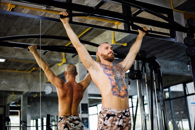 Татуированный мужчина делает упражнения в тренажерном зале