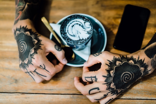 tattooed hands. hands holding a glass with coffee. 