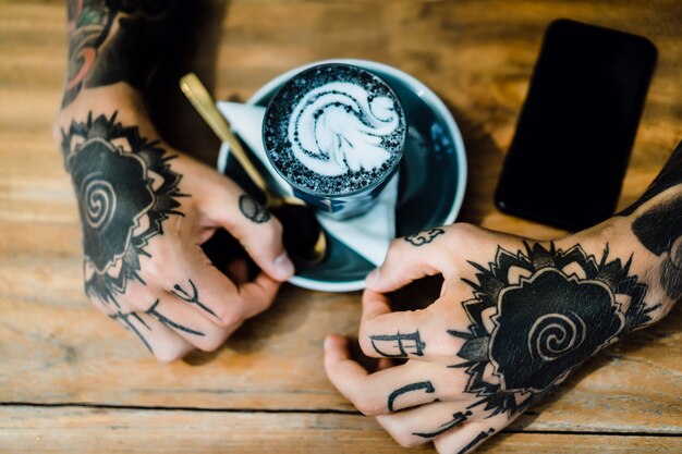 tattooed hands. hands holding a glass with coffee. 