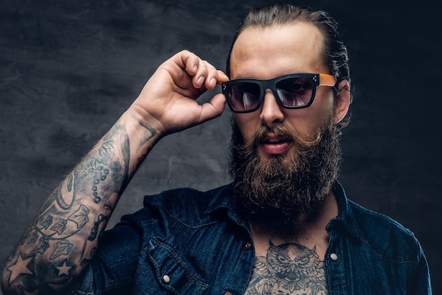 Бесплатное фото Татуированный мужчина с бородой касается солнцезащитных очков на лице.