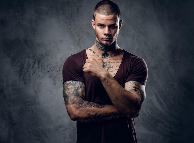Tattooed male with crossed arms over grey artistic background.