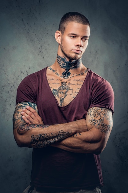 Татуированный мужчина со скрещенными руками на сером художественном фоне.