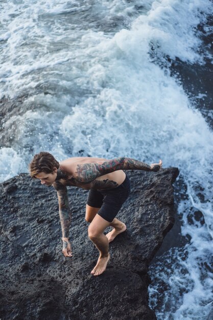 Татуированный человек лежит на краю скалы. брызги океанских волн.