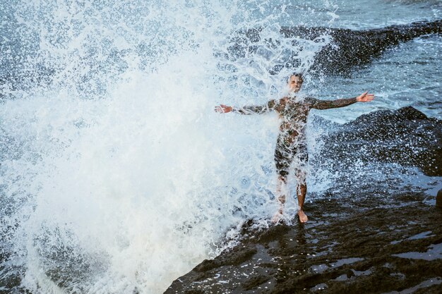 A tattooed man lies on the edge of a cliff. splashes of ocean waves.