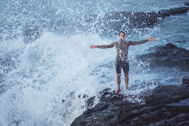 A tattooed man lies on the edge of a cliff. splashes of ocean waves.