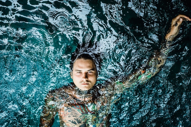 Uomo tatuato nella piscina sotto la pioggia.