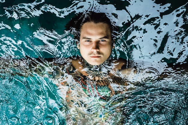 Foto gratuita uomo tatuato nella piscina sotto la pioggia.