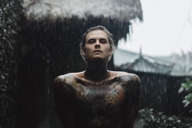 Бесплатное фото Татуированный мужчина позирует в дождь