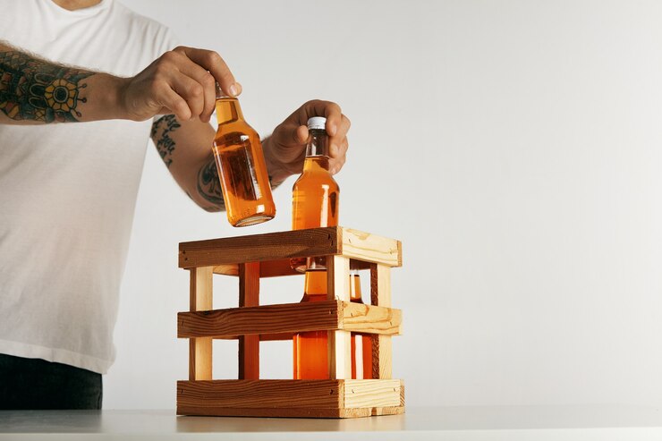 Free Photo tattooed man's hands in blank white t-shirt putting bottles with cider into a wooden crate isolated on white