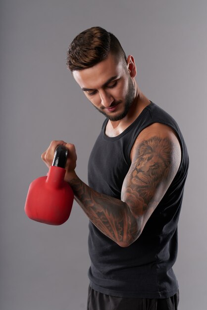Tattooed man training bicep with kettlebell