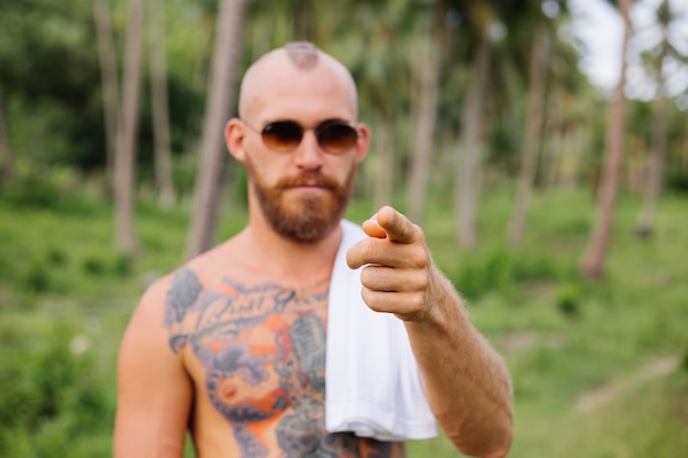 Tattooed strong man on jungle tropical field without shirt