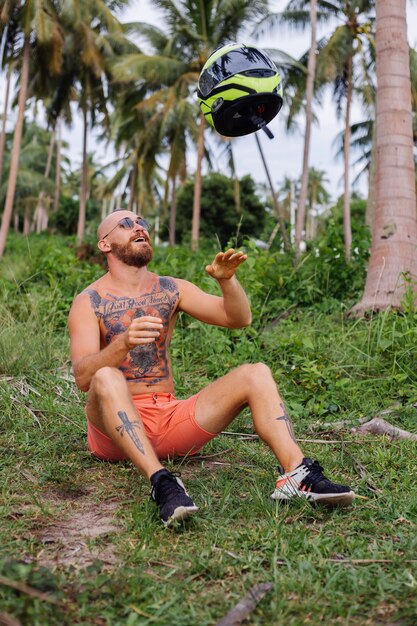 Tattooed strong man on tropical jungle field with red motorbike