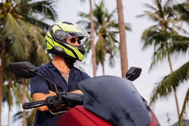 Tattooed strong man on tropical jungle field with red motorbike