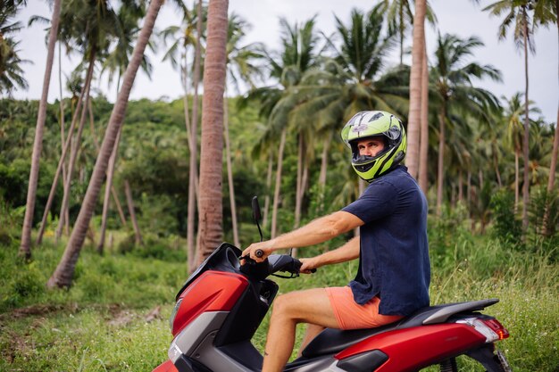 Tattooed strong man on tropical jungle field with red motorbike