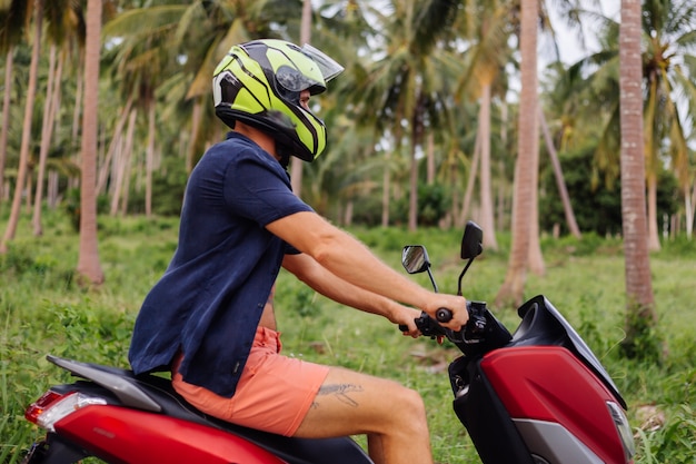 Tattooed strong man on tropical jungle field with red motorbike