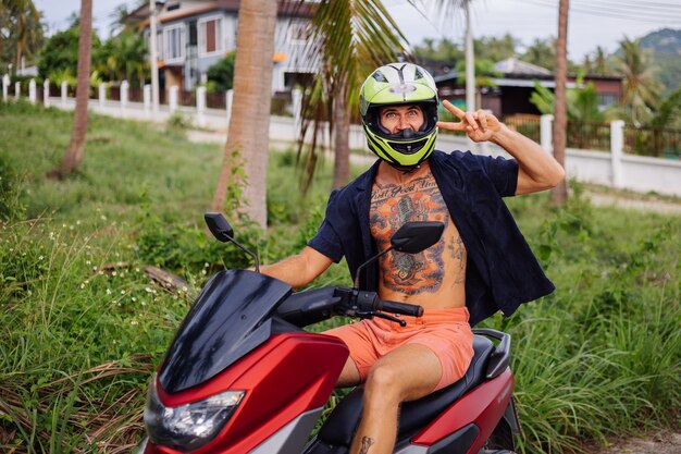 Tattooed strong man on tropical jungle field with red motorbike