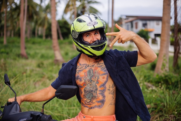 Tattooed strong man on tropical jungle field with red motorbike