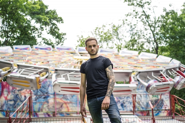 Free photo tattooed young man in an amusement park on the background of a merry-go-round