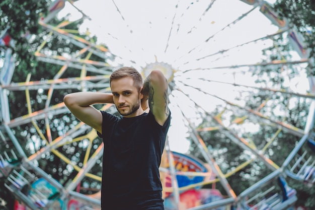 Free photo tattooed young man in an amusement park on the background of a merry-go-round