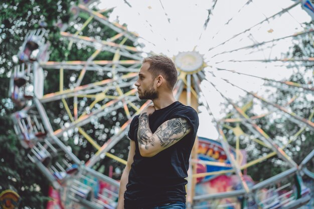 Free photo tattooed young man in an amusement park on the background of a merry-go-round