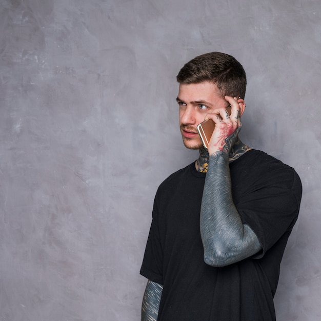 질감 된 회색 배경 휴대 전화에 문신 된 젊은 남자