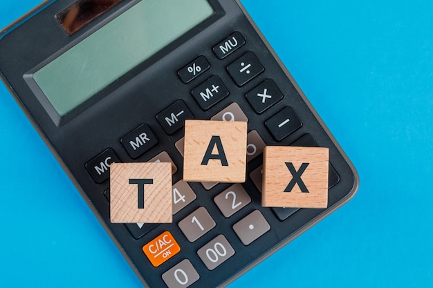 Tax planning concept with wooden cubes on calculator on blue table flat lay.