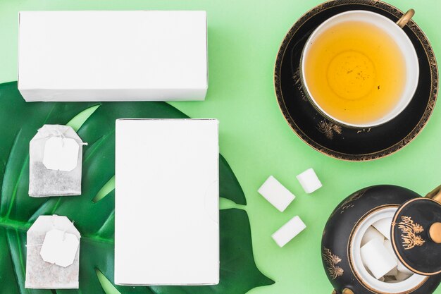 Tea bags, sugar cubes, and boxes with herbal tea cup on green background