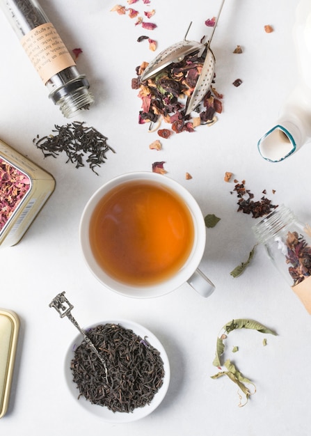 Tea cup is surrounded with different type of dried herbs on white backdrop