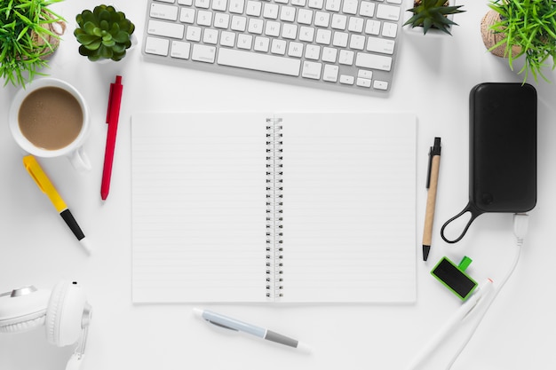 Tea cup; plant pots; spiral notepad; tea cup and pens on white desk