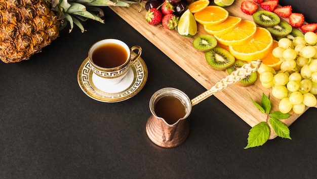 Tea cup and slices of fruits on chopping board over the black background